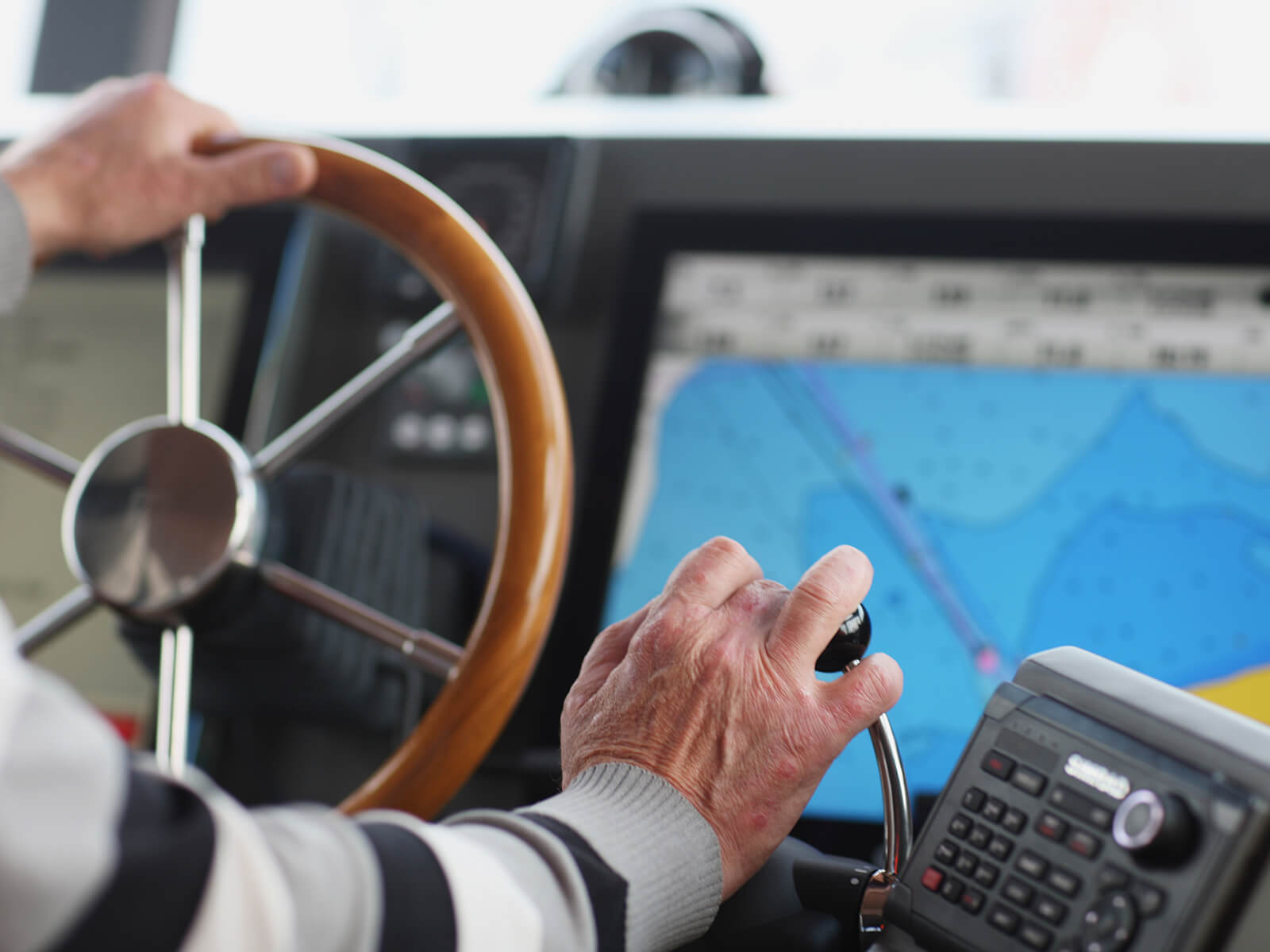 Ein älterer mann steuert eine Motor-Yacht. Der Bildschirm zeigt eine Karte mit Navigationsanzeige.