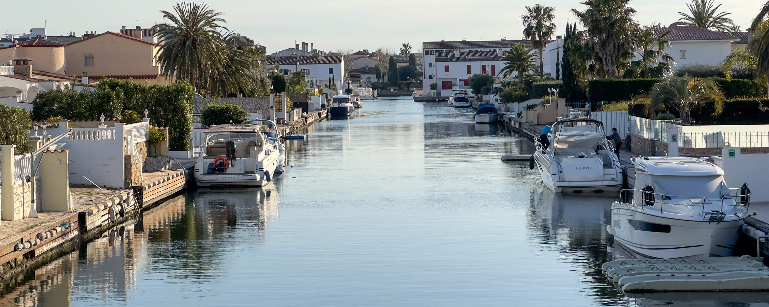 Ein breiter Wasserkanal in einer spanischen Stadt am Meer. Mehrere Boote an privaten Anliege-Stegen.